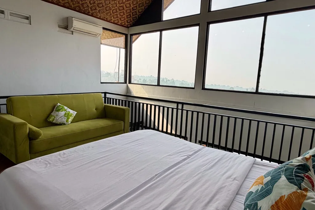 Sudut lounge Kamar 1 dengan sofa, queen bed, dan lantai kayu