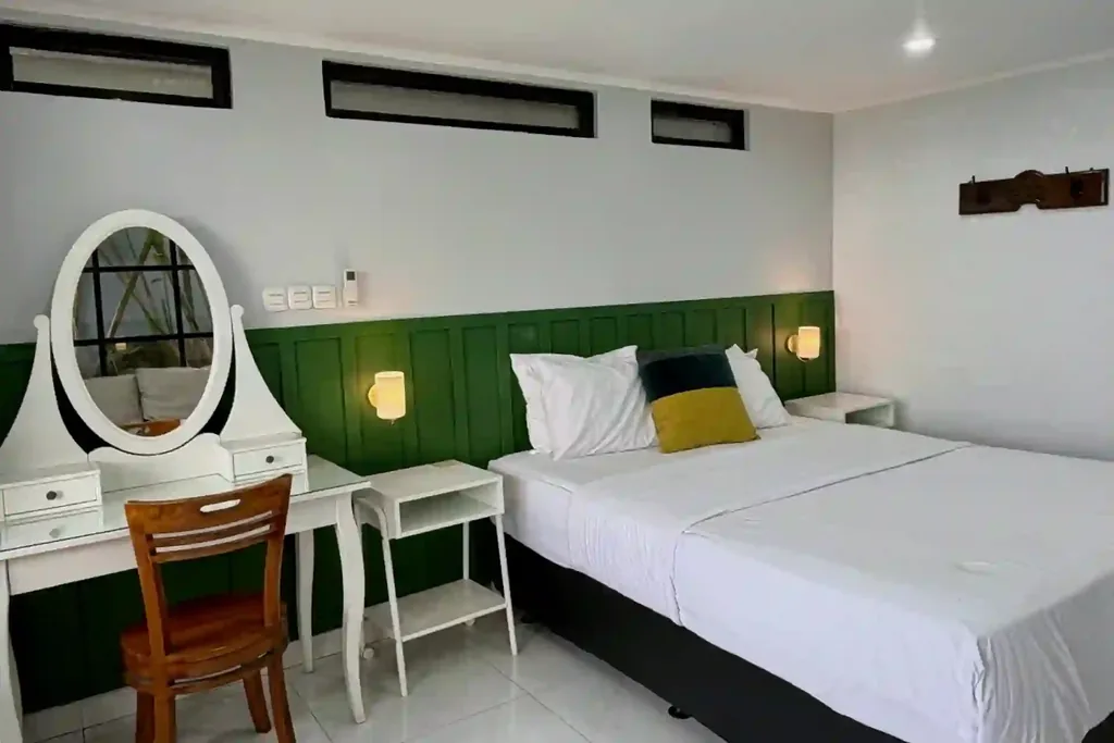 Queen bed Kamar 4 dengan headboard panel hijau, bantal mustard dan teal, serta lampu dinding