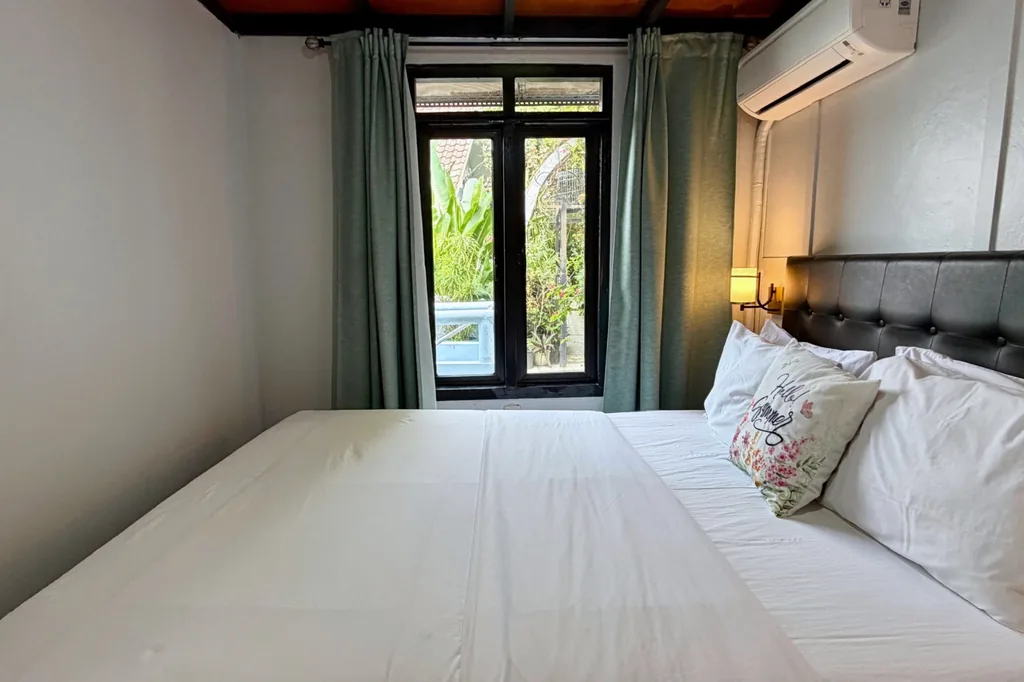 Kamar 2 Villa Yucca dengan queen bed, gorden hijau, dan jendela menghadap taman