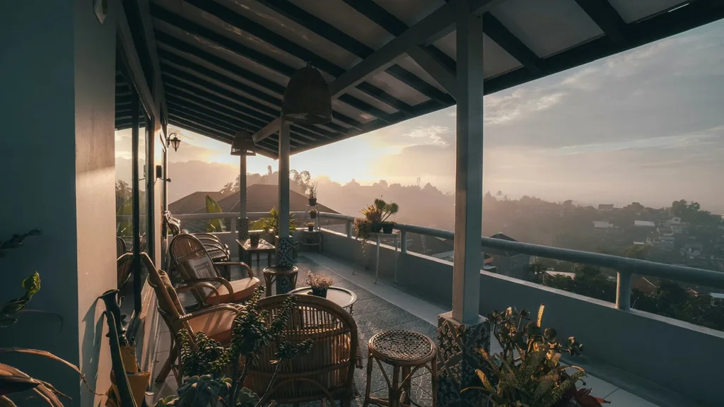 Balkon tertutup di Villa Yucca saat matahari terbit dengan kursi rotan dan kabut di atas bukit Bandung